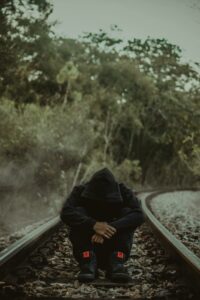 A man wearing a hoodie, sitting on an empty train track. 